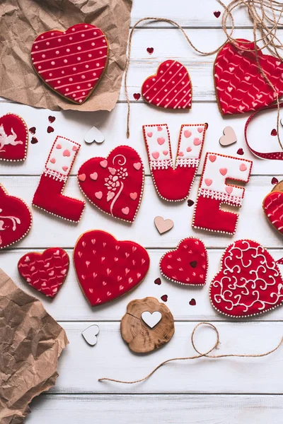 Festive composition with red glazed cookies with love lettering, paper pieces on wooden planks background for romantic day.