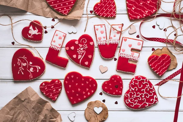 Festive composition with red glazed cookies with love lettering, paper pieces on wooden planks background for romantic day.