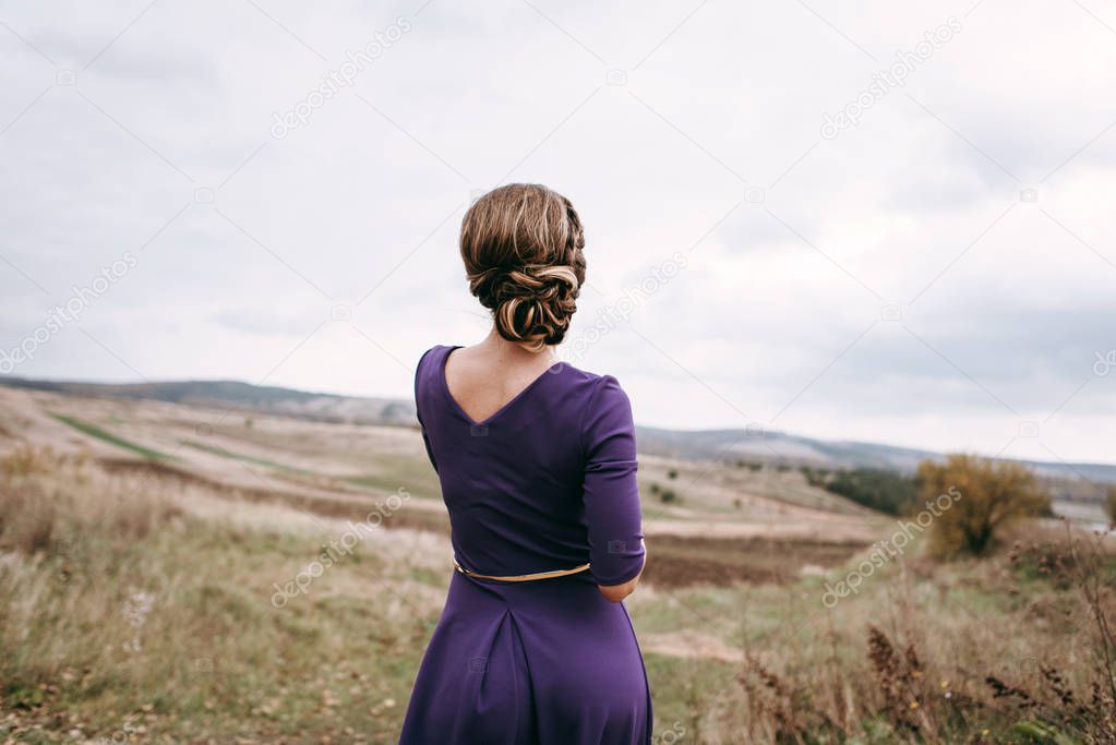 Rear view of woman wearing purple evening dress and feminine hairstyle standing in field