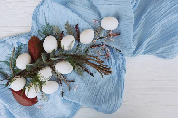 由鸡蛋 蓝色披肩 芽和茎组成的白色木板背景的花卉组合物 — 图库照片