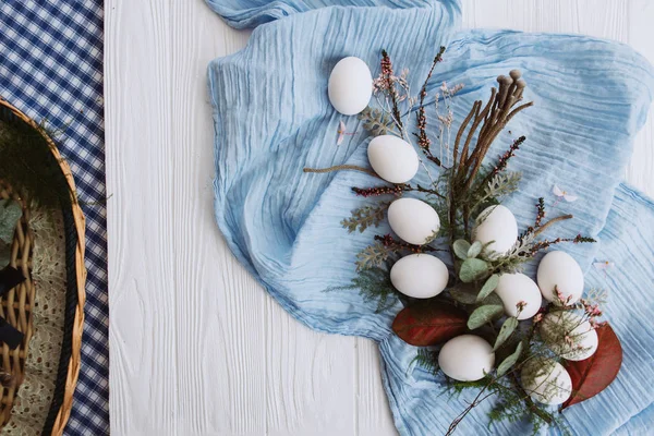 由鸡蛋 蓝色披肩 芽和茎和篮子的花朵组成的白色木板背景下的绿叶 — 图库照片