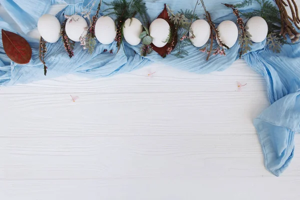 在蓝色披肩上排成一行的白色蛋的特写 上面有芽和茎 — 图库照片