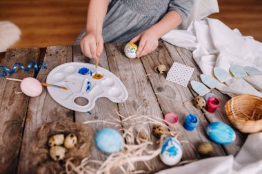 Paskalya yumurtası tutarak ve rahat Oda ahşap masada paletindeki renkleri karıştırma küçük kız görünümünü kırpılmış