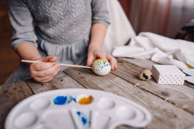 Holding ve ahşap masa, fırça, mavi ve sarı renklerle nokta yumurta boyama çocukça el kısmi görünümü