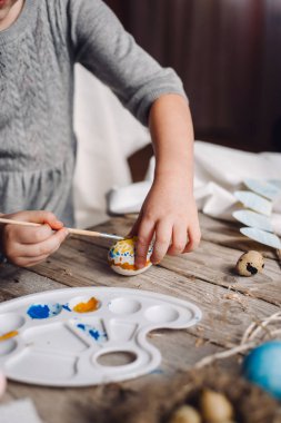 Holding ve Bıldırcın yumurta boyalar, yumurta ve palet ile ahşap masa, fırça, mavi ve sarı renklerle Boyama Çocuk kırpılmış görünümünü eller