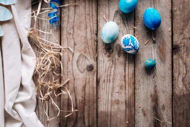Dikey ahşap plakalar arka plan üzerinde sağ tarafta, mavi kurdele, saman ve kumaş mavi renkli yumurta ile şenlikli kompozisyon Üstten Görünüm
