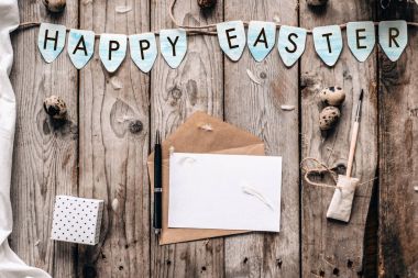 Bıldırcın yumurtası, zarf açık mektup, hediye kutusu, kalem, fırça, kumaş ve ahşap plakalar arka plan üzerinde mutlu Paskalya yazı ile mavi bayrak ile Üstten Görünüm