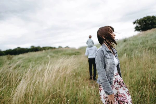 Woman enjoying windy weather and man with girl on shoulders walking on field