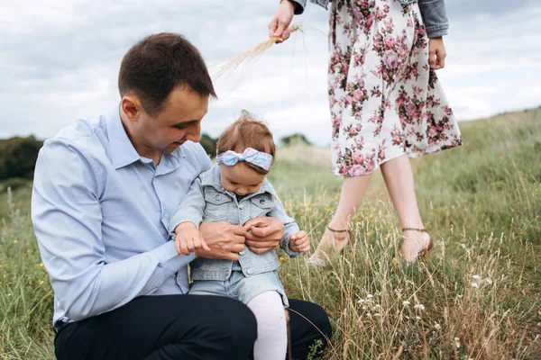 Man sitting on grass and hugging little girl and woman with wheat in hand behind