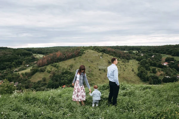 View of young family standing on field on green hills background