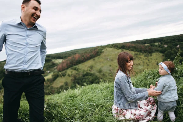 Mother with daughter sitting on grass and man running around and having fun