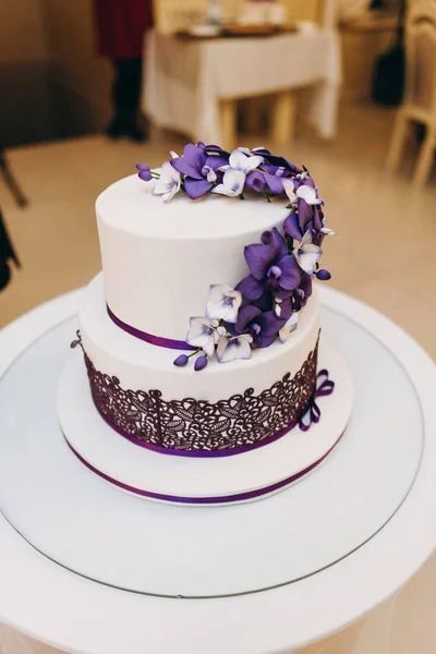 Wedding cake in white and purple colours with flowers served on white cake stand
