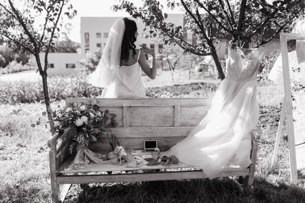 Rear view of bride with wavy hair and veil standing behind bench in garden