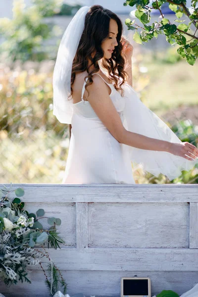 Portrait of bride with wavy hair and veil standing at bench in garden