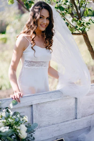 Portrait of bride with wavy hair and veil smiling and looking at camera in garden
