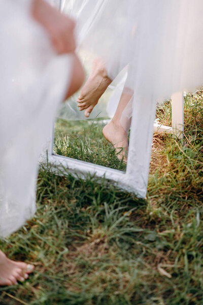 Closeup of barefoot bride standing on grass with mirror
