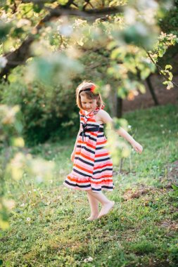 Sevimli kız çizgili elbise bahar bahçede yürüyüş