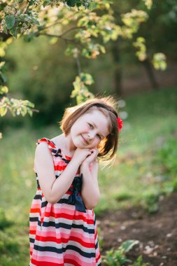 Sevimli küçük kız gülümseyerek ve çiçek açan bahçesinde kamera poz