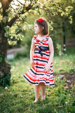 Küçük şirin kız elbise ve çiçek açan bahçede yürüyüş bandı