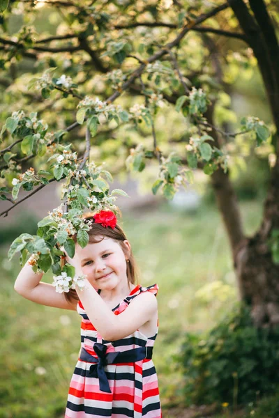 Portrait of cute girl in dress and headband posing at blooming apple tree