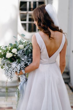 Arka görünüm portre dalgalı saç modeli ve kabarık düğün buket karşı eski beyaz bina poz ile gelinin