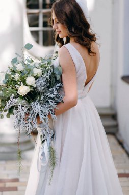 Arka görünüm portre dalgalı saç modeli ve kabarık düğün buket karşı eski beyaz bina poz ile gelinin