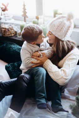 Woman with small boy cuddling on bed with decorated christmas tree on background