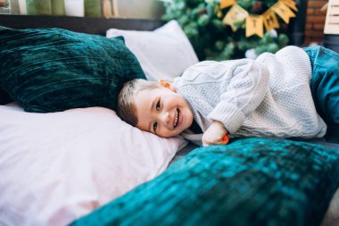 Smiling boy resting on bed with pillows