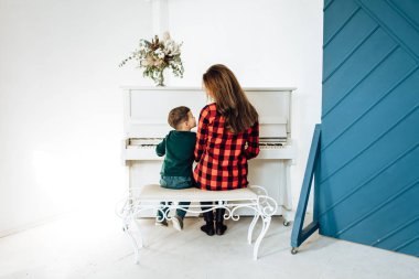 Rear view of woman with small boy plaing piano in white room