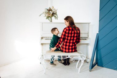 Rear view of woman with small boy plaing piano in white room