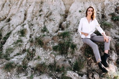 Şehvetli kadın dışarıda poz veriyor, kayanın üzerinde otları tutuyor..