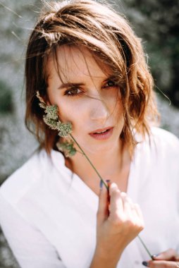 Pretty woman with natural makeup posing outdoors, playing with herbs and looking at camera.