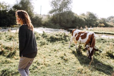 Smiling woman walking in field with cow on background