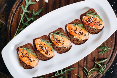 Beyaz tabakta roka ile servis edilen çavdar ekmekli ve somonlu tost.