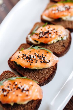 Beyaz tabakta roka ile servis edilen çavdar ekmekli ve somonlu tost.