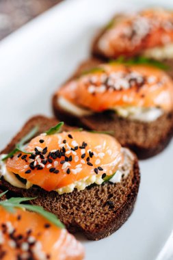 Beyaz tabakta roka ile servis edilen çavdar ekmekli ve somonlu tost.