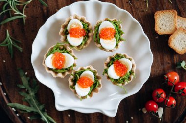 Appetizers with seaweeds, red salmon caviar and eggs served on white seashell plate
