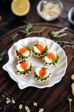 Appetizers with seaweeds, red salmon caviar and eggs served on white seashell plate