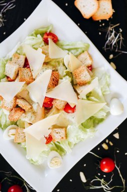 Sezar salatası beyaz tabakta ve siyah taş tahtada servis edilir.