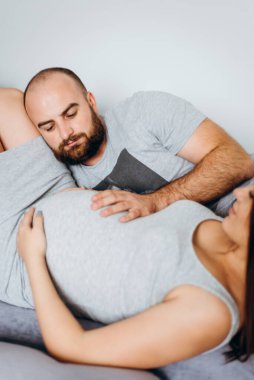 Hamilelik. Bebek bekleyen genç bir çift. Bekleyen harika anne babalar, doğum için dairelerinde kucaklaşırlar.