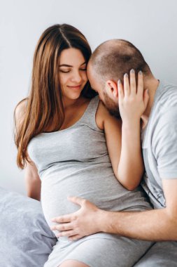 Hamilelik. Bebek bekleyen genç bir çift. Bekleyen harika anne babalar, doğum için dairelerinde kucaklaşırlar.