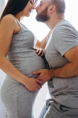 Hamilelik. Bebek bekleyen genç bir çift. Bekleyen harika anne babalar, doğum için dairelerinde kucaklaşırlar.