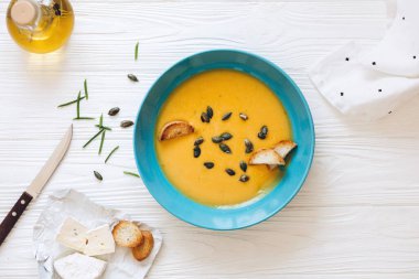 Mavi kasede ev yapımı balkabağı çorbası, kızarmış ekmek ve zeytinyağı ve peynir ile servis edilen tohumlar.