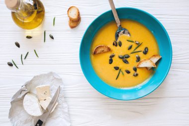 Mavi kasede ev yapımı balkabağı çorbası, kızarmış ekmek ve zeytinyağı ve peynir ile servis edilen tohumlar.