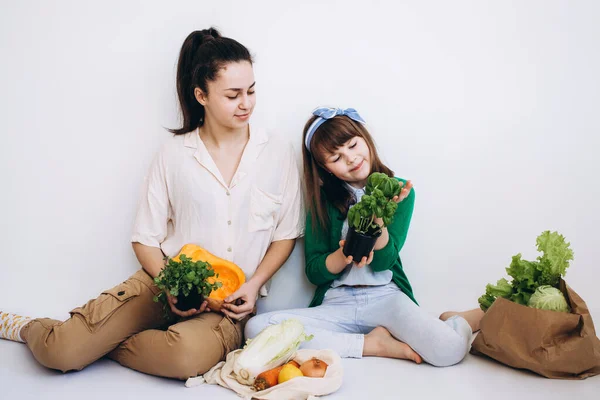 Unpacking an eco bag of fresh vegetables and greens after grocery shopping by two girls. Healthy eating concept.