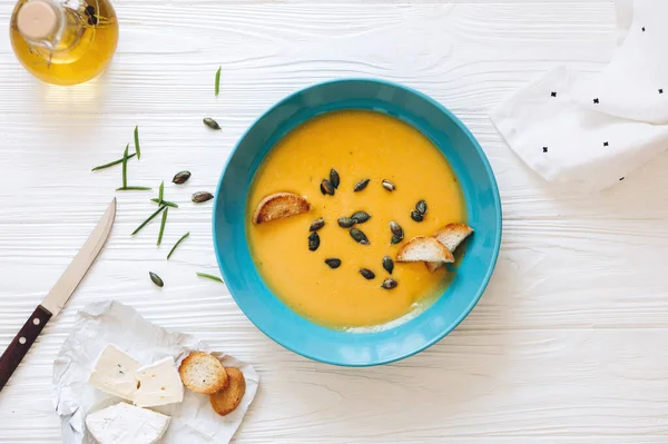 Mavi kasede ev yapımı balkabağı çorbası, kızarmış ekmek ve zeytinyağı ve peynir ile servis edilen tohumlar.