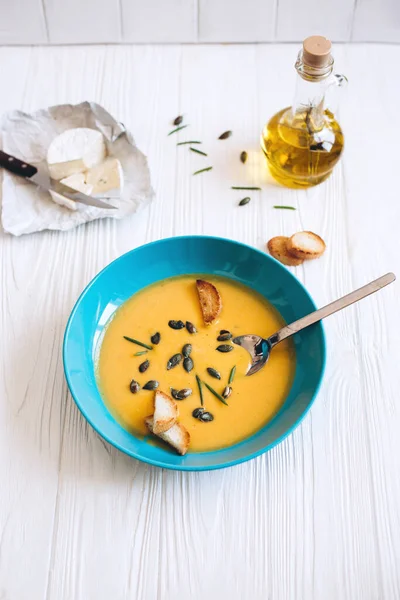 Mavi kasede ev yapımı balkabağı çorbası, kızarmış ekmek ve zeytinyağı ve peynir ile servis edilen tohumlar.