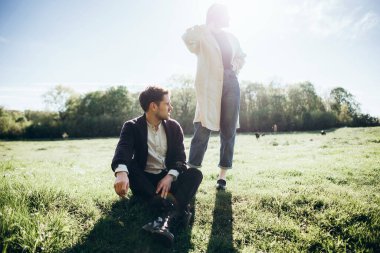 Yeşil alanda sigara içen genç adam, arka planda kadın.