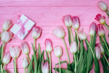 Pembe laleler pembe ahşap arka planda hediye kutusuna saçılmış.