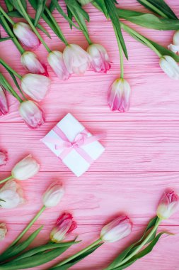 Pembe laleler pembe ahşap arka planda hediye kutusuna saçılmış.